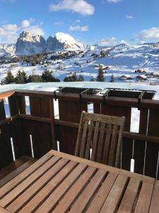 a wooden table and chair on a balcony with snow covered mountains at Appartamento con vista sull'Alpe di Siusi in Bulla