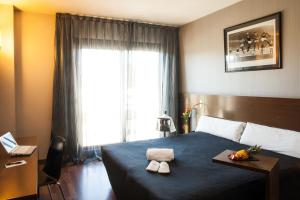 a hotel room with a bed, table, lamp and window at TaCH Madrid Airport in Madrid