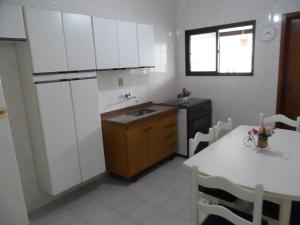 cocina con armarios blancos, mesa y fregadero en T004 - Apto na Tupi com sacada, garagem e ótima localização, en Samaritá 7 fotos más