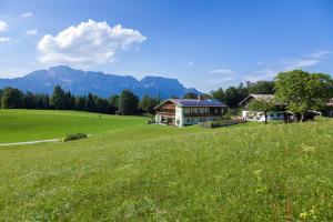 ein Haus auf einem grünen Feld mit Bergen im Hintergrund in der Unterkunft Gästehaus Lärcheck Berchtesgaden FeWo Wiesentraum in Berchtesgaden