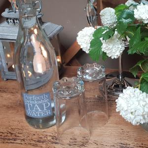 uma garrafa e dois copos numa mesa com flores em Scaldersitch Farm Boutique Camping Tipi with private wood fired hot tub em Sheen