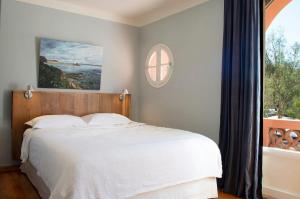 a bedroom with a white bed and a window at Hôtel Le Porquerollais in Porquerolles