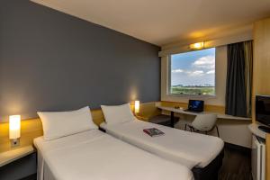 Habitación de hotel con 2 camas, escritorio y ventana en ibis Vitoria Aeroporto, en Vitória