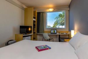 a hotel room with a bed and a desk and a window at ibis Vitoria Aeroporto in Vitória