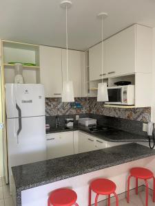 une cuisine avec des placards blancs et des tabourets rouges dans l'établissement Flat no Nannai Residence, à Porto de Galinhas