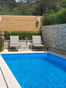 a swimming pool with two chairs and a stone wall at Apartment Natasa in Rab