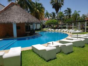 a resort swimming pool with white chairs and a straw umbrella at VILLA ACAPULCO DIAMANTE in Acapulco