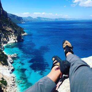 a person sitting on a cliff looking at the ocean at Biriola EcoResort Cala Gonone in Cala Gonone
