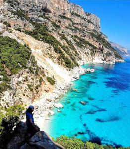 a man sitting on a cliff looking at the blue ocean at Biriola EcoResort Cala Gonone in Cala Gonone