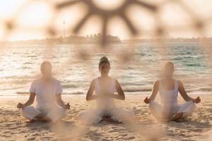 three women sitting in meditation on the beach at Taj Exotica Resort & Spa, The Palm, Dubai in Dubai