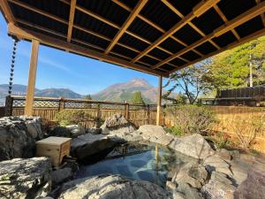 a hot tub in a garden with mountains in the background at Yufuin-Sanso Waremokou in Yufu