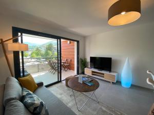 a living room with a couch and a tv and a table at L'ORANGERAIE - Garage, Balcon, Vélos, Proche Lac, Vue Montagne in Annecy