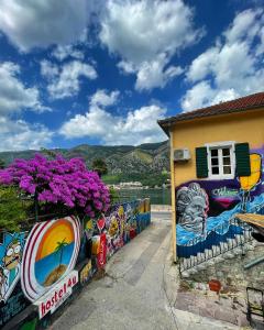 Montenegro Hostel 4U في كوتور: لوحة جدارية على جدار بجوار مبنى به زهور أرجوانية