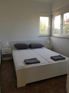 ein weißes Bett in einem weißen Zimmer mit zwei Fenstern in der Unterkunft Vila Mila Apartments in Sukošan