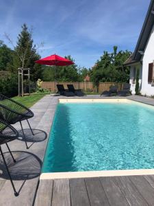 a swimming pool with chairs and a red umbrella at Les Chambres Chez Christine in Ottrott