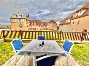 une table et des chaises sur une terrasse avec une clôture dans l'établissement Résidence La Ferme de Deauville - Saint Arnoult, à Saint-Arnoult