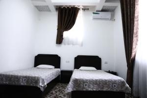 duas camas num quarto com paredes brancas e cortinas em Demir Hotel Bukhara em Bucara