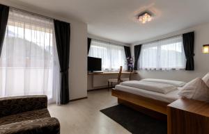 a bedroom with a bed and a chair and windows at Garni Sunela B&B in Selva di Val Gardena