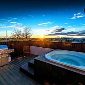 - un bain à remous sur une terrasse avec vue sur le coucher du soleil dans l'établissement ICELAND SJF Villa, Hot tub & Outdoor Sauna Amazing Mountains and City View Over Reykjavík, à Reykjavik