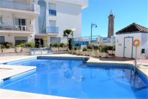 a swimming pool in front of a building with a lighthouse at Estepona Port Luxury Apartment AURA in Estepona