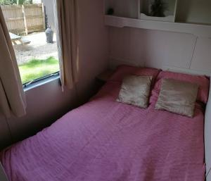 a small bedroom with a pink bed with two pillows at Poplar Lodge Log Caravan in Kirkby on Bain