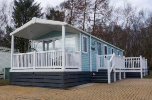 a blue tiny house with a white porch and a porch at Silver Birch Retreat - Percy Woods Country Retreat With 18 HOLE FREE GOLF in Alnwick