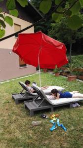 due persone sdraiate sui letti sotto un ombrello rosso di Apartma Opalika a Cerkno (Circhina)