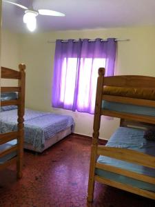 a bedroom with two beds and a window with purple curtains at Prainha Pousada - Bar e Restaurante in Itanhaém