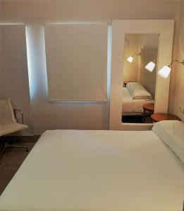 a bedroom with a large white bed and a mirror at Hotel Oromana in Alcalá de Guadaira