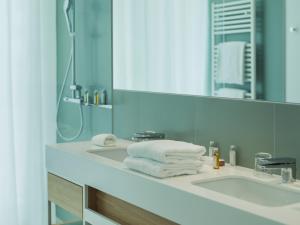 a bathroom with a sink with a mirror and towels at Falkensteiner Residences Jesolo in Lido di Jesolo