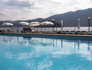 a swimming pool with umbrellas and chairs and the water at Hotel San Rocco in Orta San Giulio