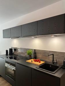 une cuisine avec des armoires noires et un évier avec des tomates sur une planche de découpe dans l'établissement Apartmenthaus Stade Schwingewiesen Apartment 3, à Stade