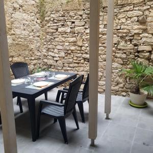una mesa negra y sillas en un patio con una pared de piedra. en Appart 40m2 indépendant, confortable avec terasse, en Lunel