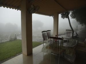 a porch with a table and chairs in the rain at Ashoka Villa 3 BHK Mahabaleshwar in Mahabaleshwar