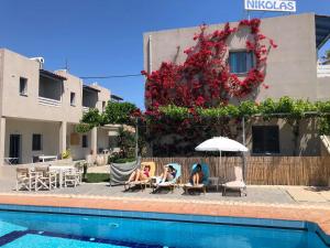 two women sitting in chairs next to a swimming pool at Nikolas Apartments in Amoudara Herakliou