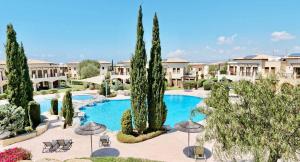 a resort with a large swimming pool with trees and umbrellas at Pool side ground floor apartment BF02 - Theseus Village, Aphrodite Hills Resort in Kouklia