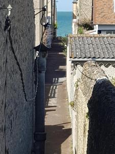 una pared de piedra junto a una calle con el océano en Le ptit passage en Saint-Aubin-sur-Mer