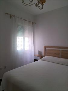 ein Schlafzimmer mit einem weißen Bett und einem Fenster in der Unterkunft APARTAMENTO EN URBANIZACIÓN AL-ÁNDALUs CERCA DE LA PLAYA DE LA BARROSA in Chiclana de la Frontera
