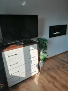 een witte dressoir met een flatscreen-tv en een plant bij Wygodny apartament blisko morza in Łokciowe