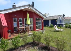 un cottage rouge avec un chien assis dans la cour dans l'établissement Strandpark 11, à Grömitz