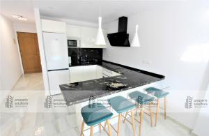 una cocina con encimera negra y taburetes azules en Pueblo del parque 12 - Terraza - Piscina y Playa- Urbanización tranquila- Perfecto para descansar, en Benalmádena