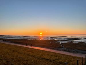 a sunset over the ocean with people walking on the beach at Ankertau in Norden