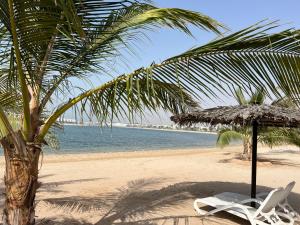 a beach with a palm tree and a chair and an umbrella at Relaxing villa with access to pool and beach in Ras al Khaimah