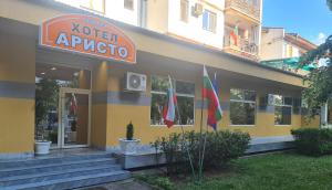 a yellow building with flags in front of it at Семеен хотел Аристо in Dryanovo