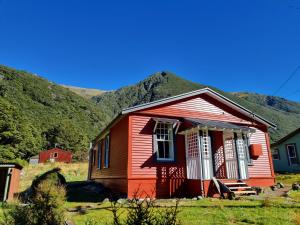 a small red house with mountains in the background at The Tussocks, Arthur's Pass in Arthur's Pass