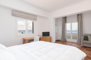 a white bedroom with a bed and a desk and window at Hotel Roumani in Spetses