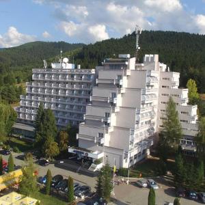 Hotel Montana - Covasna في كوفزنا: مبنى ابيض كبير وامامه موقف