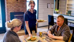 een vrouw die een man bedient aan een tafel in een restaurant bij Wellnesshotel Spabron in Wachtum