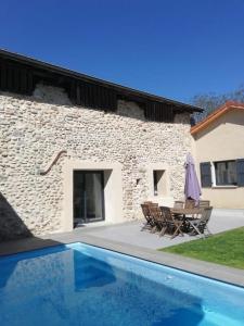 een stenen huis met een tafel en stoelen en een zwembad bij La grange au pied du Vercors Piscine et SPA privatifs in Saint-Romans