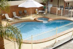 uma grande piscina com cadeiras e um guarda-sol em Courtyard Motor Inn em Shepparton